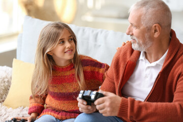 Little girl with her grandfather playing video game at home