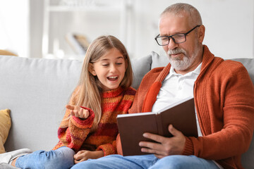 Little girl with her grandfather reading book at home