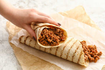 Woman holding tasty burrito on light background