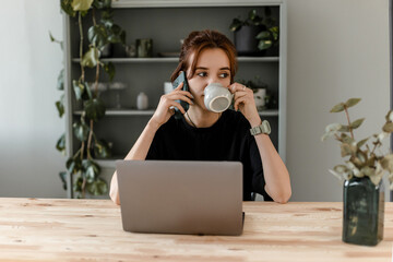 A girl with a mug works at a computer at home. Work at home