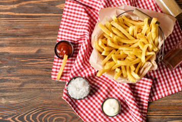 Basket with tasty french fries and sauces on wooden background