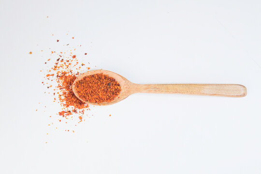 Red chili flakes on a wooden spoon on white background