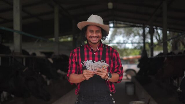A dairy farmer smilingly counts the cash in his hand. There is a background of a dairy farm.