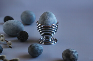 Easter painted egg in a metal stand with eggs and willow on a blue background