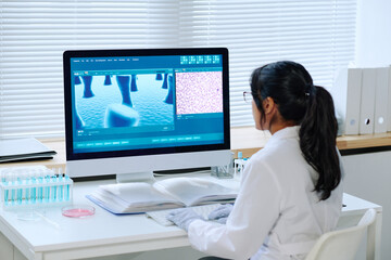 Young contemporary virologist studying characteristics of new strain of coronavirus while sitting...