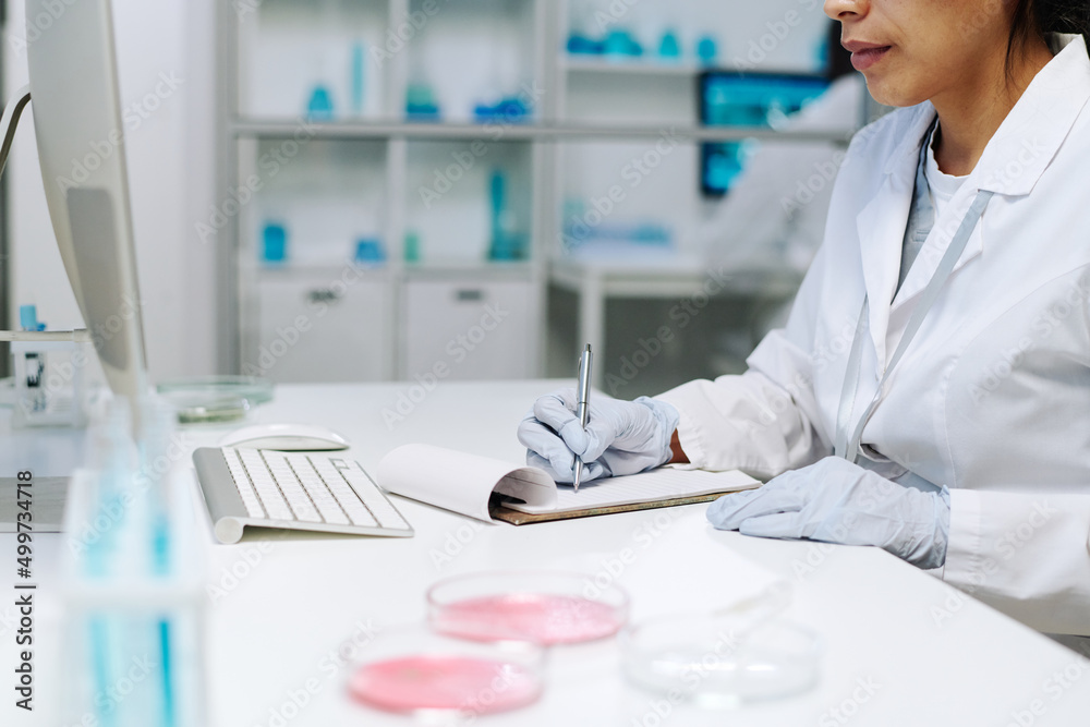 Aufkleber gloved hands of young female scientist in whitecoat making notes in clinical document while sitting 