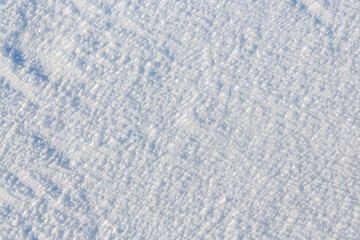 Natural snow texture. The surface of an icy snow crust. Snowy ground. Winter background with snow patterns. Perfect for Christmas and New Year design. Closeup top view.