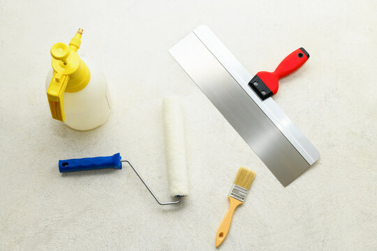 Paint set: roller, brush, spatula and liquid sprayer on the concrete floor, close-up. Repair tools lies on floor