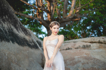 Fototapeta na wymiar Woman wearing short glitter dress enjoying romantic moment at the beach, standing near big rock.