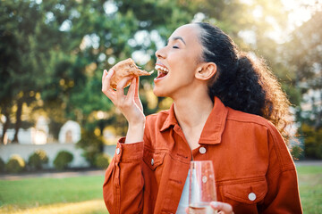 A little snack and bubbles. Shot of a young woman eating pizza in a park.
