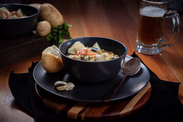 Seafood Soup in a black plate on wooden surface with a glass of beer