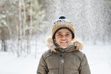 Cheerful little boy of African ethnicity wearing warm winter jacket and beanie hat while having fun...