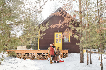 Naklejka premium Contemporary family of parents and little son in winterwear standing by their country house located in deep woods among pinetrees