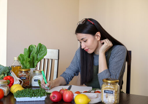 Young Asian woman writes down recipe for a dish in notebook. Zero waste. Vegetarian woman.