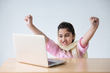 muslim girl using a laptop computer and raised hand for celebrating good news on the table
