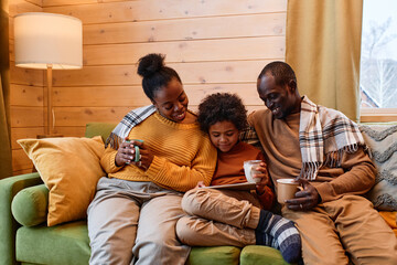 Obraz premium Young restful family watching online movie in tablet while sitting on couch in living room of their country house in the evening