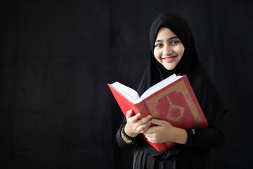 muslim girl reading a holy book quran on black background