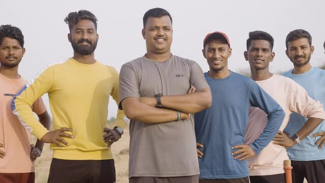 Handheld pan shot of group of college cricket team players confidently standing by looking at camera at playground - concept of treamwork, sports tournament and champions.