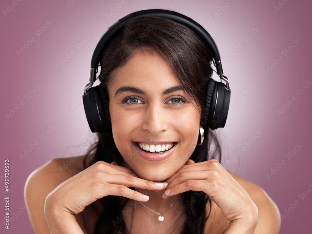 Sticker Where words fail music speaks. Shot of a beautiful young smiling woman with her hands rested on her chin while wearing headphones against a pink background.