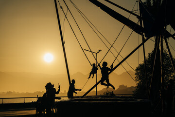 children jumping in trampoline high into the sunset sky safed with elastic safety belt