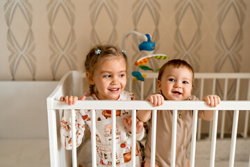 sister and her little brother sitting together in the crib, lifestyle