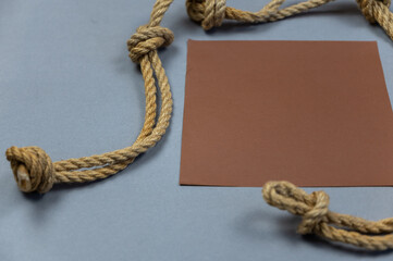 A ship's rope with knots and a brown empty square against a gray background. View from above at an angle. Close-up. Selective focus.