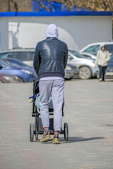 Obraz premium A man with a baby stroller walks on the sidewalk on a spring day