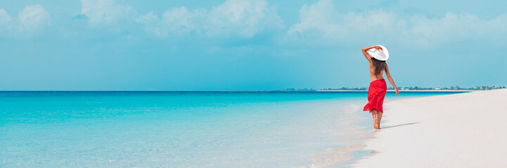 Beach vacation woman walking on summer travel Caribbean holiday wearing white sun hat and sarong...