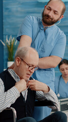 Medical assistant consulting disabled man with stethoscope for heartbeat measurement and examination. Nurse doing healthcare consultation with senior patient sitting in wheelchair