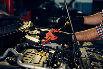 Car mechanic checking oil level in a mechanical workshop