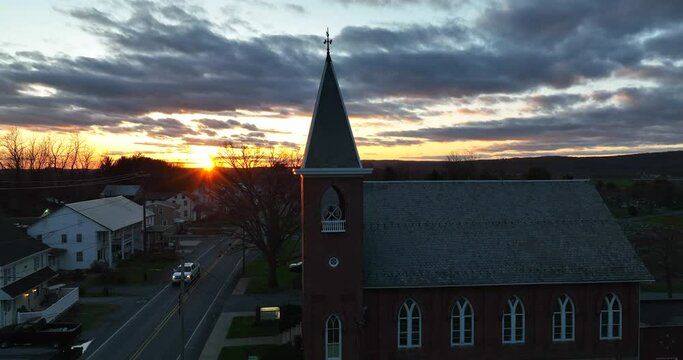 Church in rural community in USA at sunset. Truck with headlights on drive by at night. Winter sunset aerial.