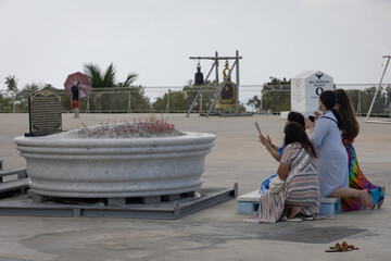 three dark-haired women kneeling in pray in front of a statue of Buddha