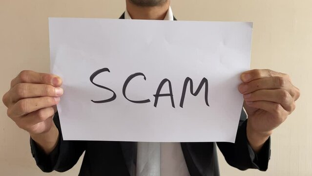 Frustrated asian male businessman professional crumpling paper with written message &ldquo;SCAM&rdquo; word. Man in suit and tie having nervous breakdown furiously throwing crumpled paper in office at work