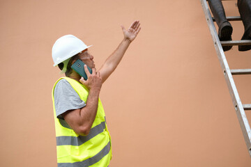 Surprised and angry foreman talks on the phone while gesturing with his hands.