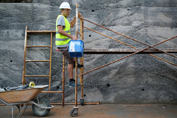worker with a bucket in his hand climbs up a scaffold.