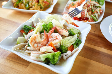 Stir Fried Mixed Vegetables and Oyster Sauce with Shrimp on wooden dining table. The fork is poking up the shrimp. Thai food.