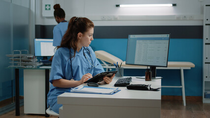 Medical assistant typing on tablet screen and checking computer for appointment in doctors office....