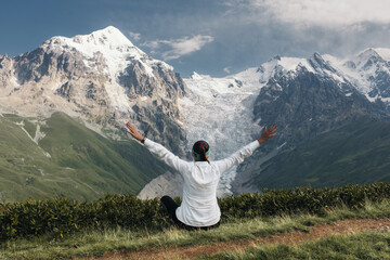 Girl hiker in white shirt spread her arms feeling free. Hiker in Svaneti on a background of the main Caucasus ridge and snow-capped mountain peaks.