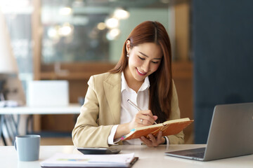 Happy young Asian businesswoman is sitting smiling and taking notes happily in the office.