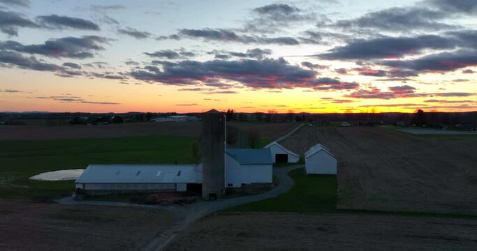 American farm rural farmland scene at sunset. Silo barn and home silhouette. Ag industry theme. Buildings painted white.