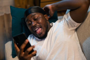A man is relaxing on the couch holding his phone. Boy reads text message on smartphone, good news, great information, joy, laughter, smile.