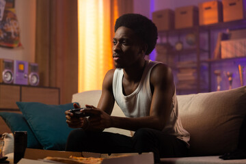 An athletic man in a white T-shirt relaxes after work playing the console, holding a pad in hands, the boy has a focused serious face, men's room