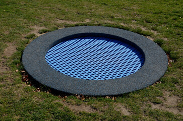 blue rubber surface of the playground with a lawn and circular trampolines sunk into the terrain. children can jump and do somersaults and various tricks in the park behind the house.