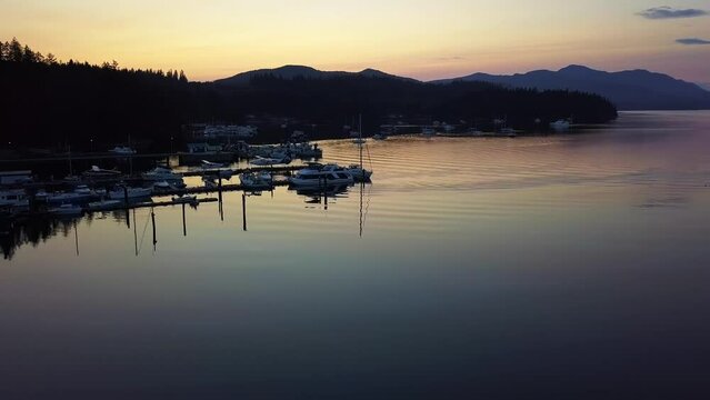 Marina Full of Boats and Seaplanes During Sunset With the Silhouette of the Mountains in the Background in Sechelt Inlet British Columbia Canada - Forward Panning Aerial Shot