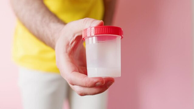 Defocused man zips up his pants and shows a close-up of a jar with a sample of semen for analysis. The concept of sperm donation.