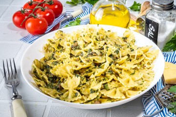 Italian mediterranean lunch concept. Farfalle pasta with spinach, mushrooms, vegetables and creamy sauce. On a white tile table, with spices for dinner copy space