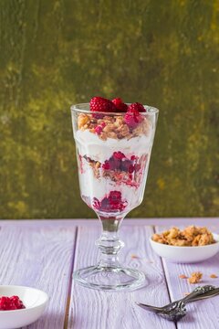 Scottish dessert Cranachan made of raspberries, oatmeal or granola and whipped cream in a glass goblet on a purple wooden background.