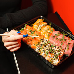 Bright sushi on a  black and red background, female hands holding a sushi sticks