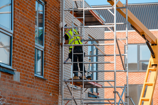 Construction workers using aluminium mobile scaffold tower and safety harness to work at height. Working at height safety regulation