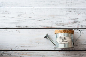 Metal silvery watering can with the inscription Home and flowers on a white wooden background. The concept of ecology, farming, gardening © Kiryakova Anna